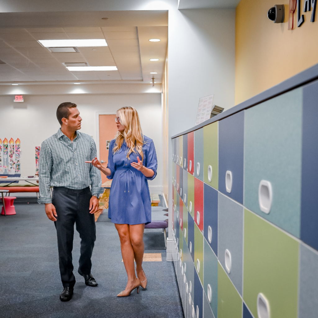 Father and Female Teacher in an open, carpeted classroom with colorful lockers at a parent/teacher conference