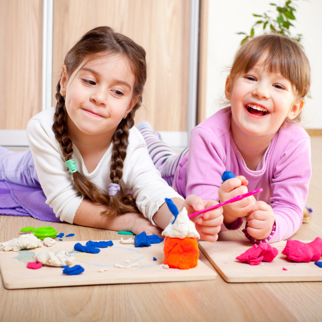 Attentions spans vary by age. Tow kindergarten girls playing with playdough. One is not focused on the camera.